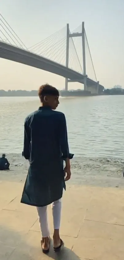 Man walking by a riverside with a large bridge in the background.