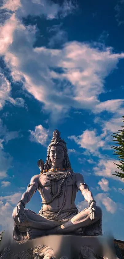 Statue of Shiva against a blue sky with clouds, evoking peace.