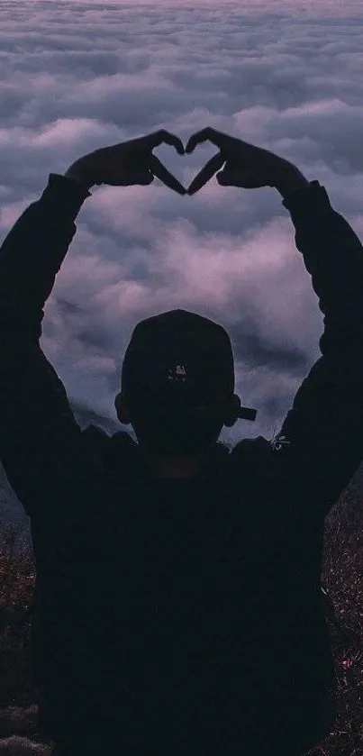 Silhouette heart gesture at sunset above clouds.