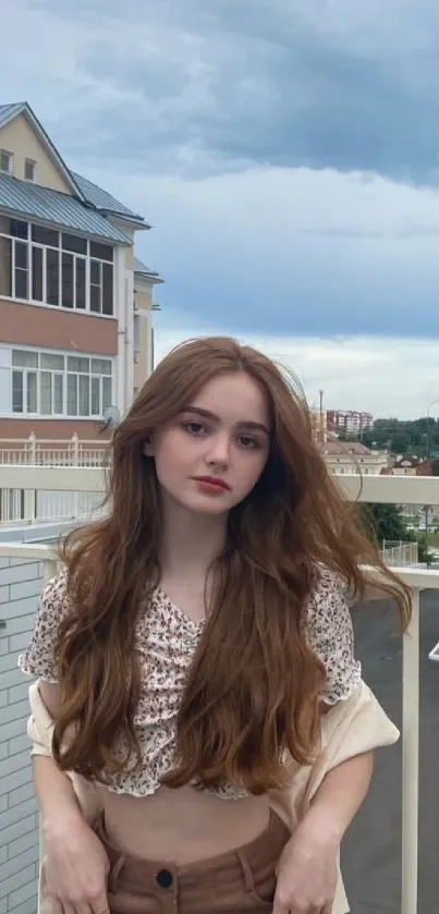 Young woman standing on a balcony with a cloudy sky background.