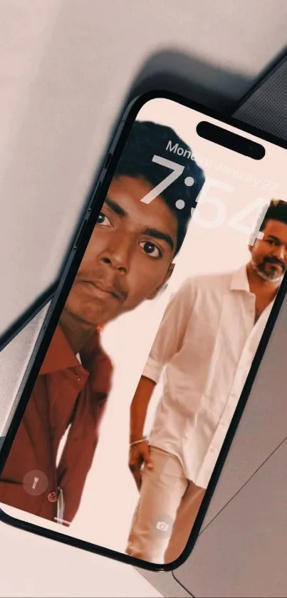 Mobile wallpaper with two men on a phone screen, lying on a laptop.