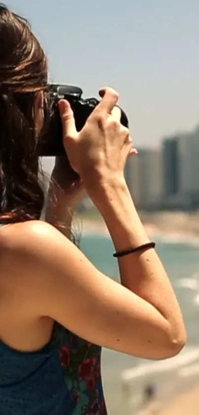 Woman photographing the ocean with city skyline in background.