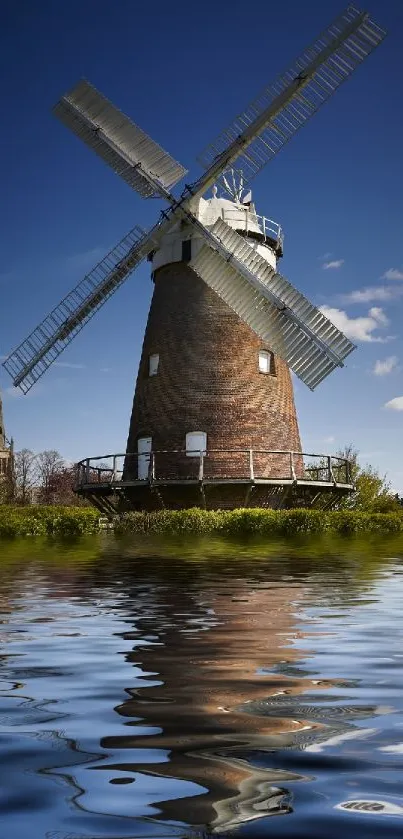 Windmill reflecting in a serene pond under a clear blue sky.