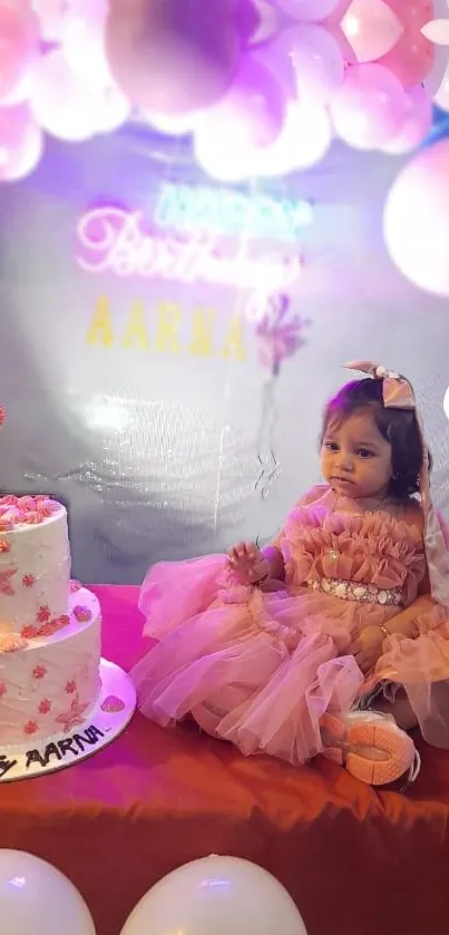 Baby in pink dress with cake and balloons at birthday party.