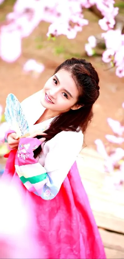 Woman in traditional attire amidst pink blossoms, smiling.