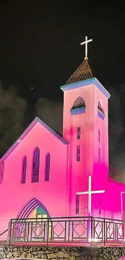 A glowing pink church illuminated beautifully at night, with parked cars nearby.