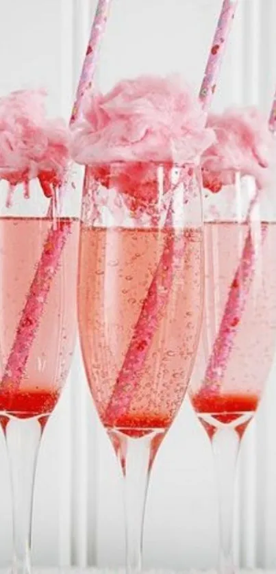 Three champagne flutes with pink cotton candy on top and pink striped straws.