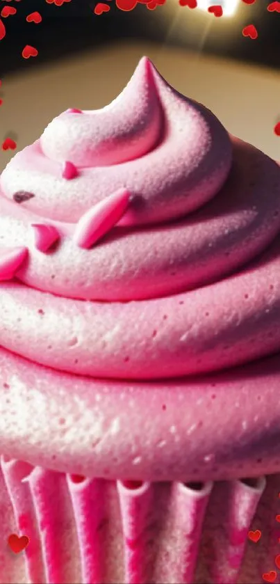 Pink frosted cupcake with heart decorations on wallpaper.