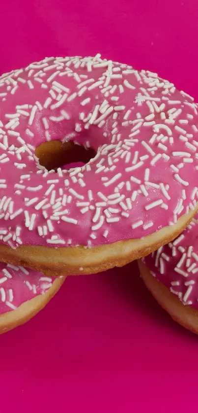 Pink frosted donuts with sprinkles on a hot pink background.