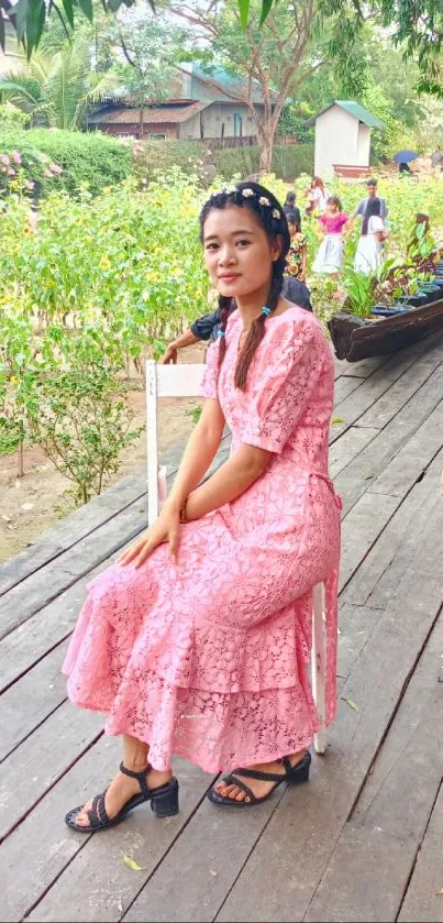 Woman in pink lace dress sitting in a lush garden setting.