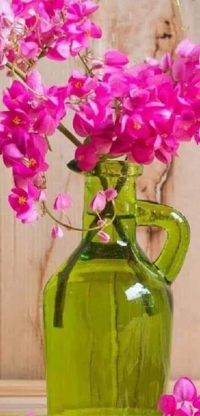 Vibrant pink flowers in a green glass vase on wooden table.