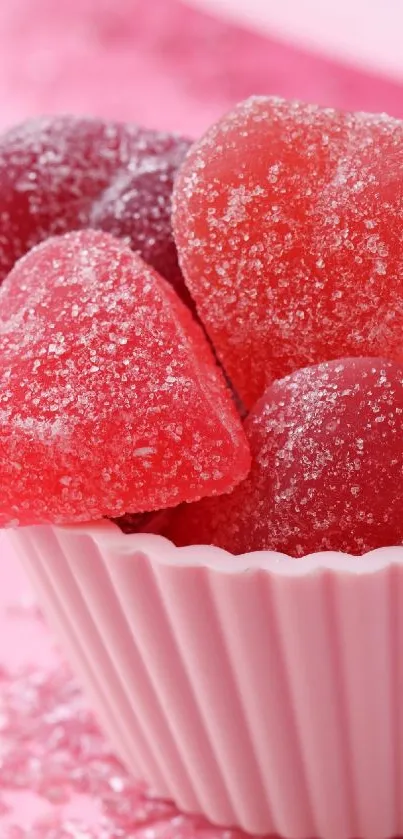 Pink sugar-coated heart candies in a white cup on a pink background.