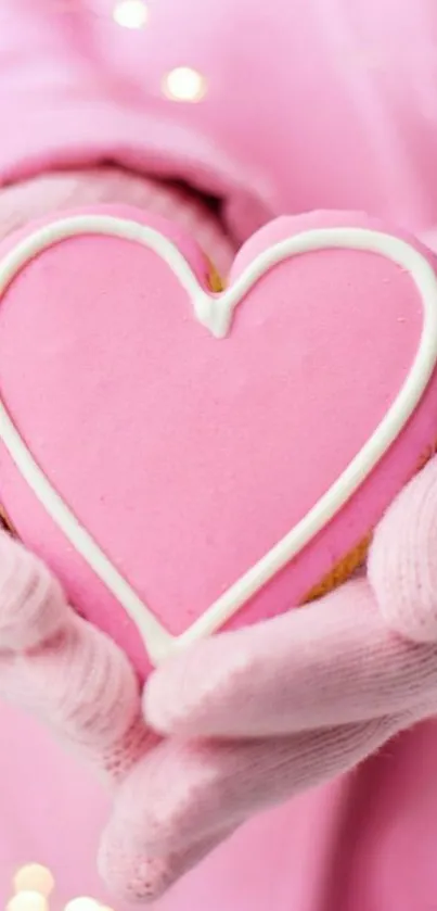 Gloved hands holding a pink heart cookie.