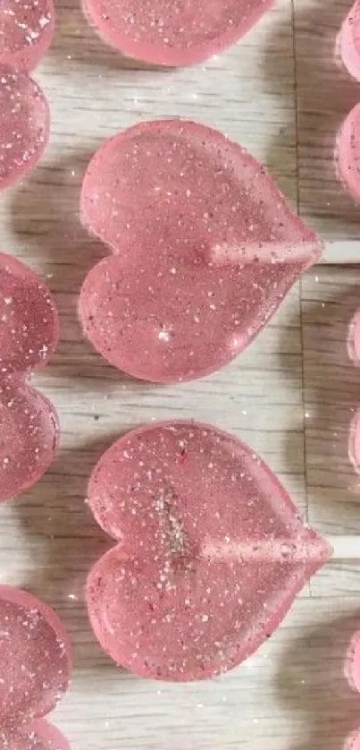 Pink heart-shaped lollipops with glitter on a wooden background.