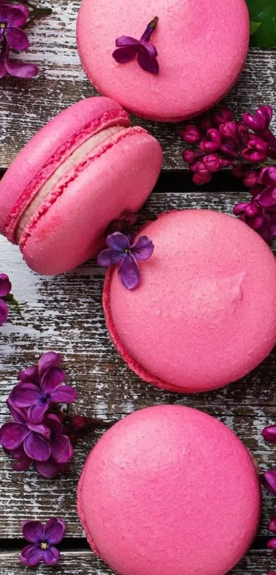 Pink macarons among purple flowers on wood.