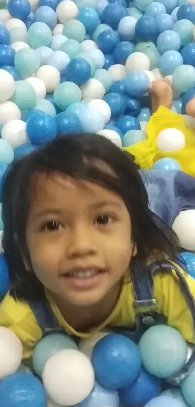 Child smiling joyfully amidst colorful play balls in a ball pit.