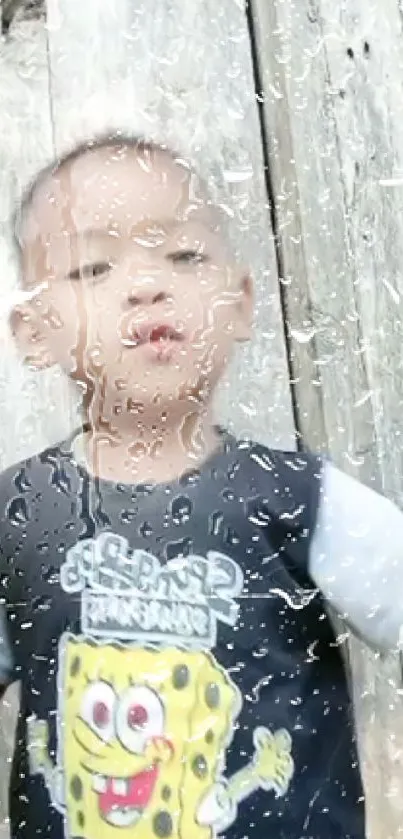 Child standing behind a rain-covered window with a cartoon shirt.