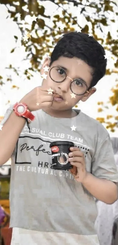 Young child with glasses outdoors holding a toy camera.