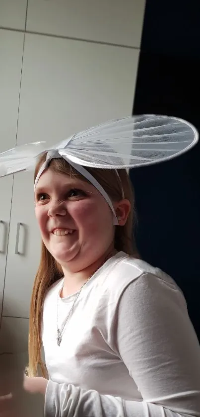 Girl wearing whimsical fairy wings indoors, smiling playfully.