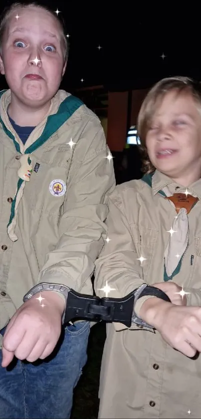 Two kids playfully handcuffed and smiling.