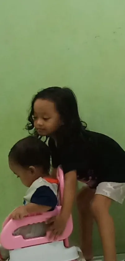 Two kids playing in front of a green wall, capturing a joyful moment.