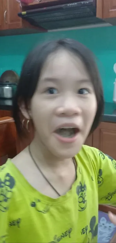 Girl in green shirt looking surprised in a cozy kitchen setting.