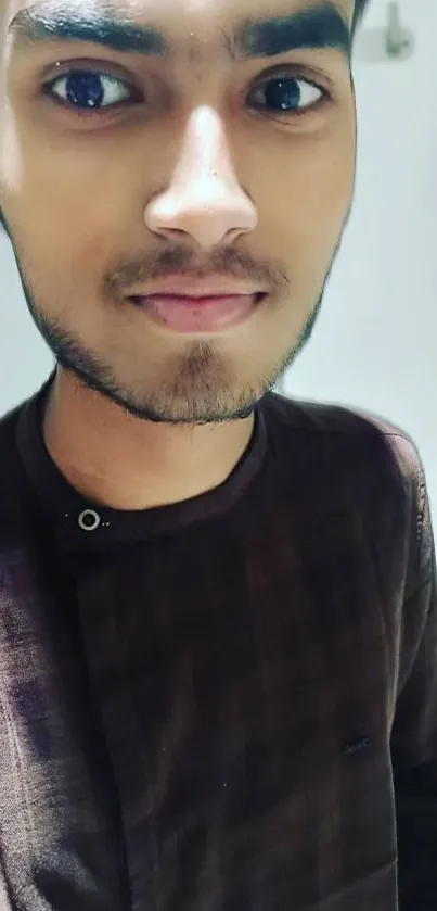 Portrait of a young man in a brown checked shirt against a light background.