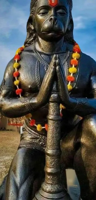 Hanuman statue in prayer with vibrant garland, peaceful mobile wallpaper.