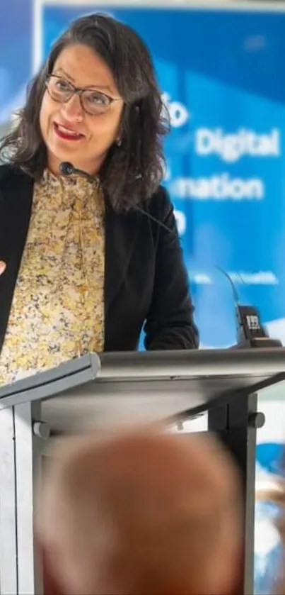 Professional woman speaking at podium with blue background.