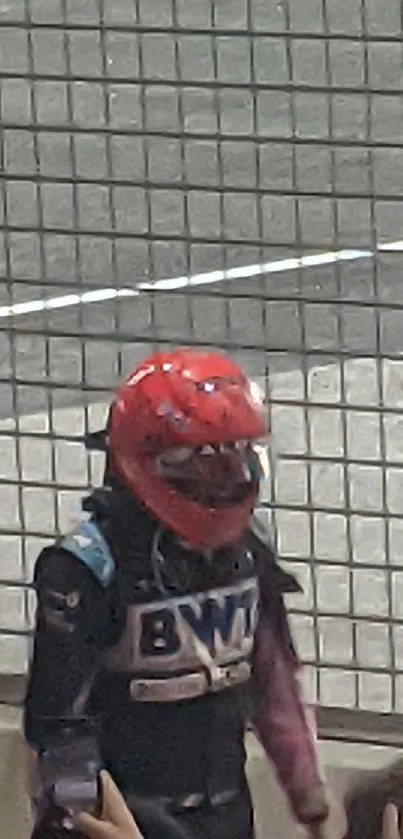 Racer in vibrant red helmet by track fence.