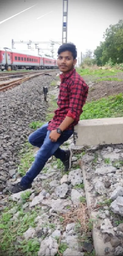 Person in red shirt sitting by train tracks with nature background.