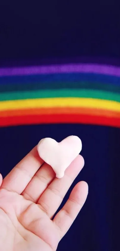 Hand holding heart with rainbow background on wallpaper.