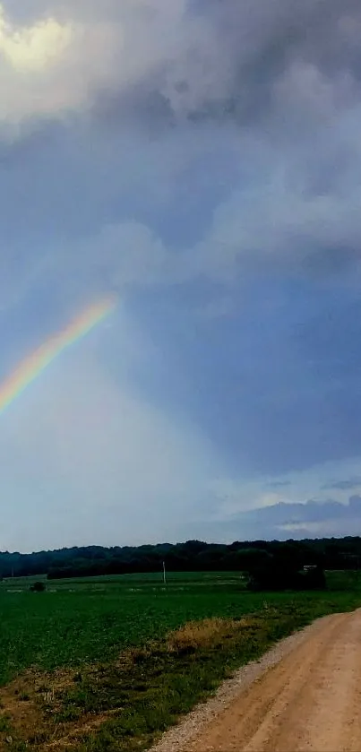 Scenic wallpaper of a rainbow over a country road and green fields under a cloudy sky.