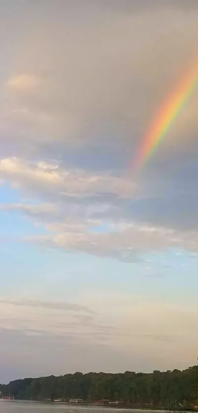 A vibrant rainbow arcs over a peaceful lake under a blue sky.