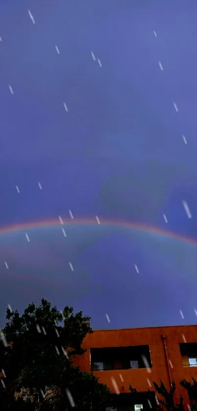 Rainbow arches over urban building against deep blue sky at twilight.