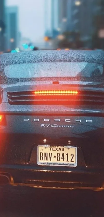 Porsche 911 Carrera driving in rainy cityscape with lights aglow.