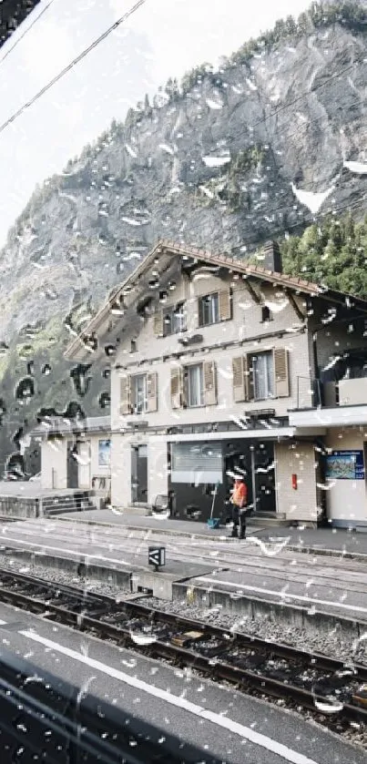 Train station view with raindrops on a window and mountains in the background.