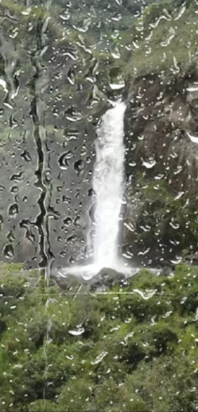 Rainy window view of a waterfall surrounded by lush green scenery.