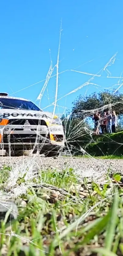 Rally car drives on dirt road, surrounded by blue sky and green scenery.