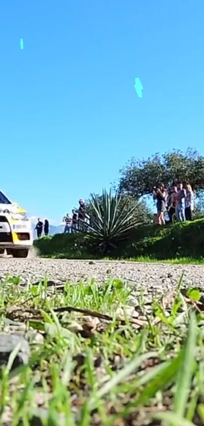 Rally car races on gravel path beneath clear blue sky.