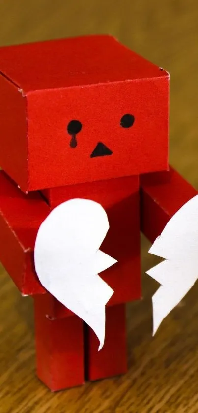 Red cardboard robot holding broken heart.