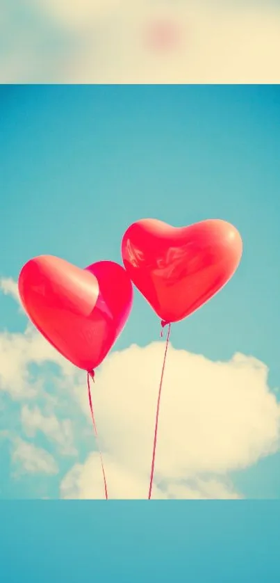 Two red heart balloons floating in a blue sky with white clouds.