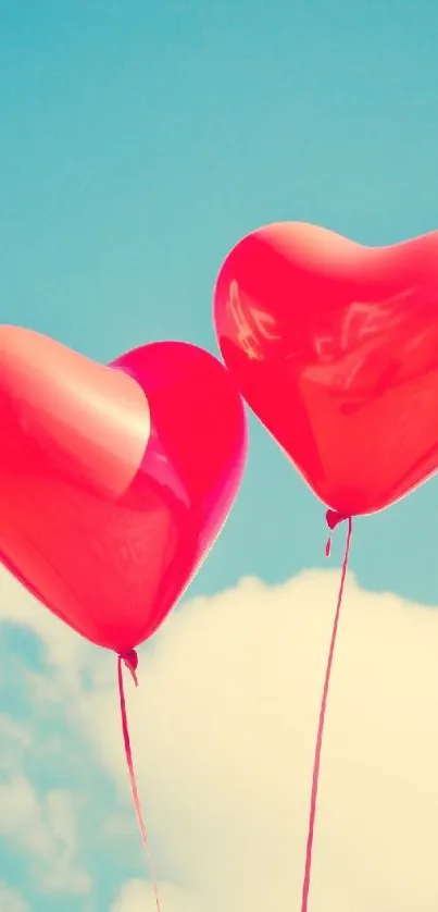 Two red heart balloons float in a clear blue sky.