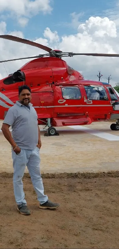 Red helicopter parked on a grassy helipad under a vibrant blue sky.