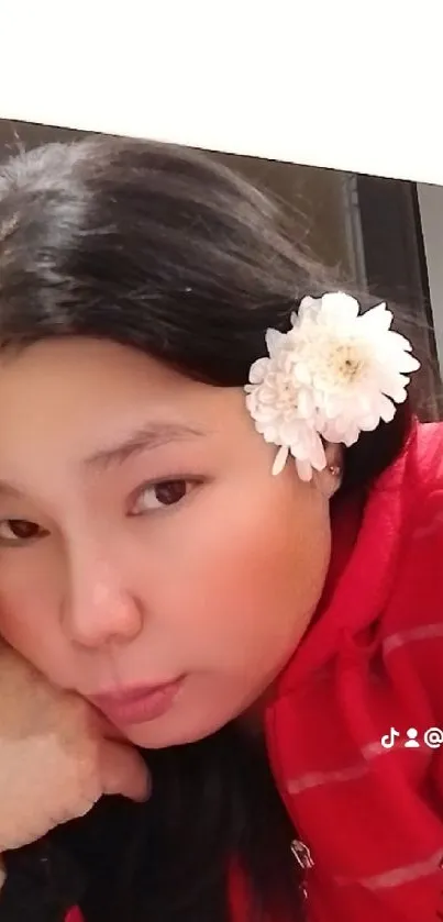 Woman in red hoodie with white flower in hair.