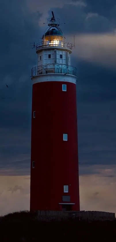 Red lighthouse illuminated against a dark evening sky.