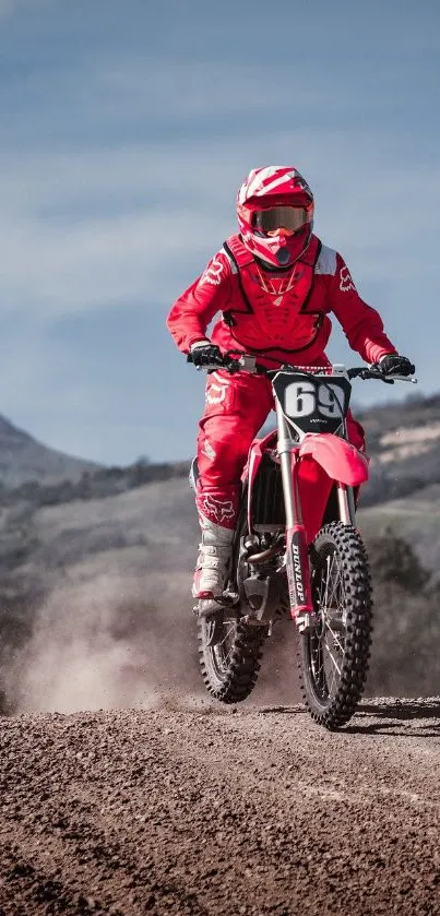 Motocross rider in red gear on a dusty track with scenic mountain backdrop.