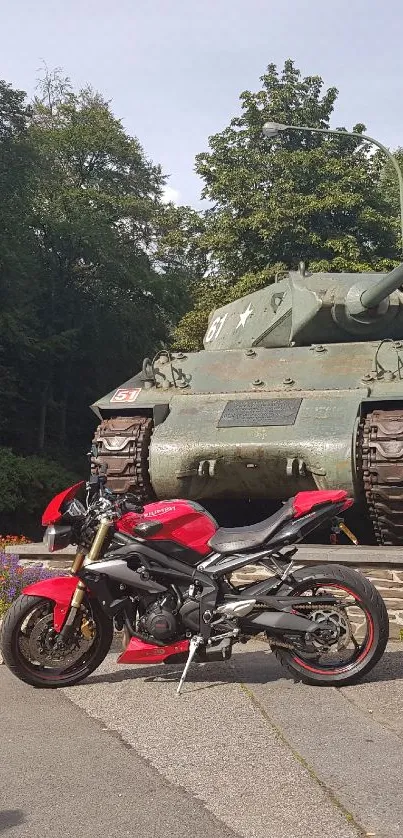 Red motorcycle parked in front of vintage tank surrounded by lush greenery.