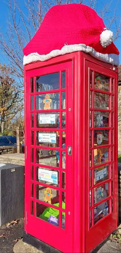 Festive red phone booth with Santa hat in sunny setting.