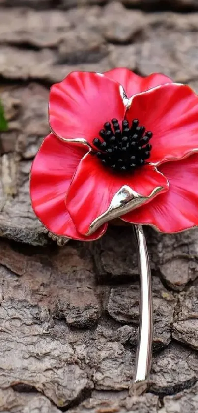 Red poppy brooch on rough bark background with green leaves.